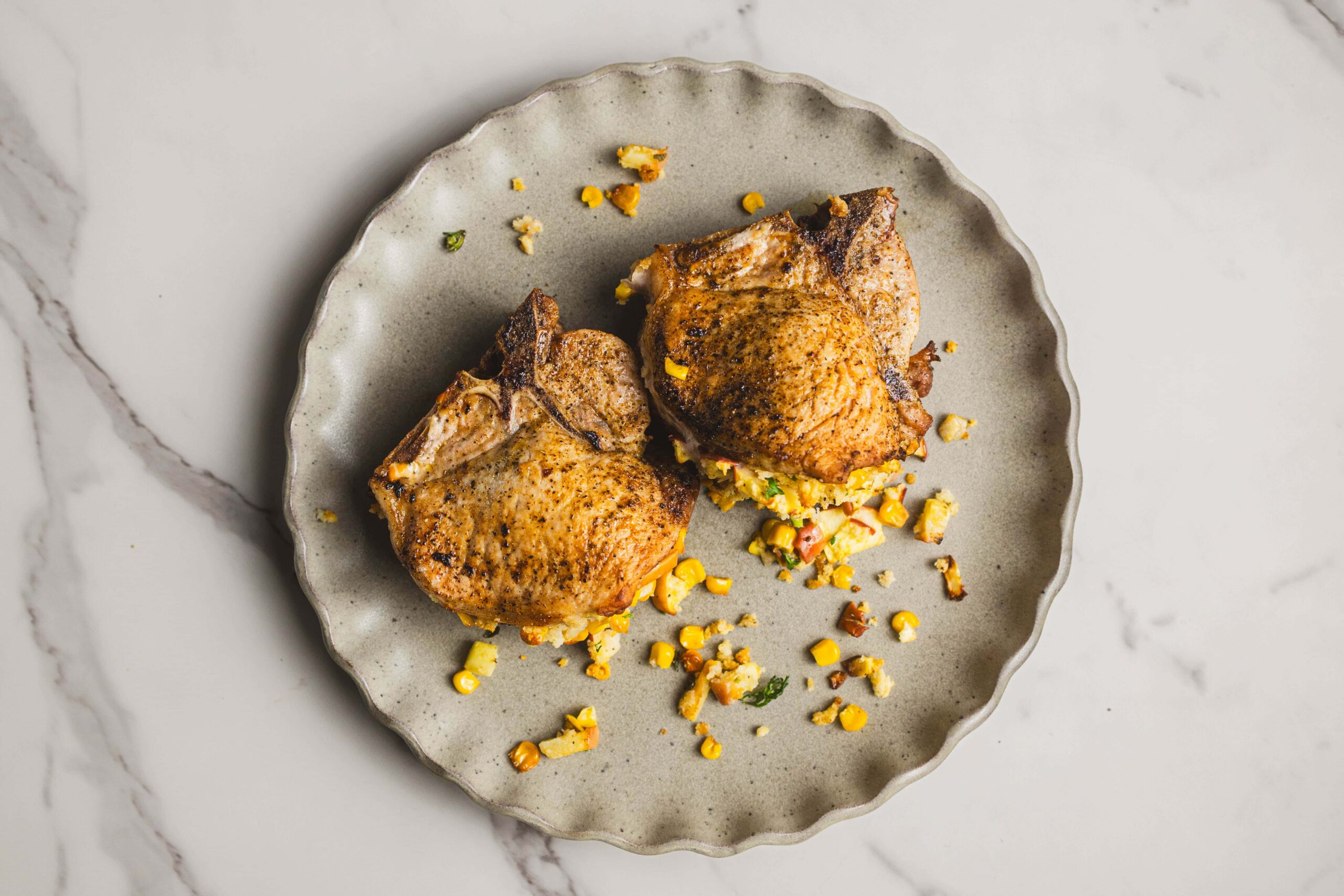 Juicy baked chicken thighs served with a fresh vegetable and corn stuffing, garnished with chopped herbs on a rustic ceramic plate. Perfect for a flavorful and hearty meal.
