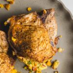 Roasted chicken thighs with crispy skin served on a rustic grey plate, paired with colorful corn and vegetable stuffing, perfect for a delicious homemade meal.