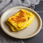 Savory scrambled eggs, golden-brown and cooked to perfection on a white plate, served as a delicious breakfast or brunch option.
