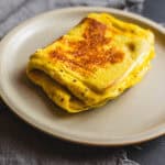 Perfectly cooked scrambled eggs with a golden-brown crust, served on a beige plate; a delicious and protein-rich breakfast option.