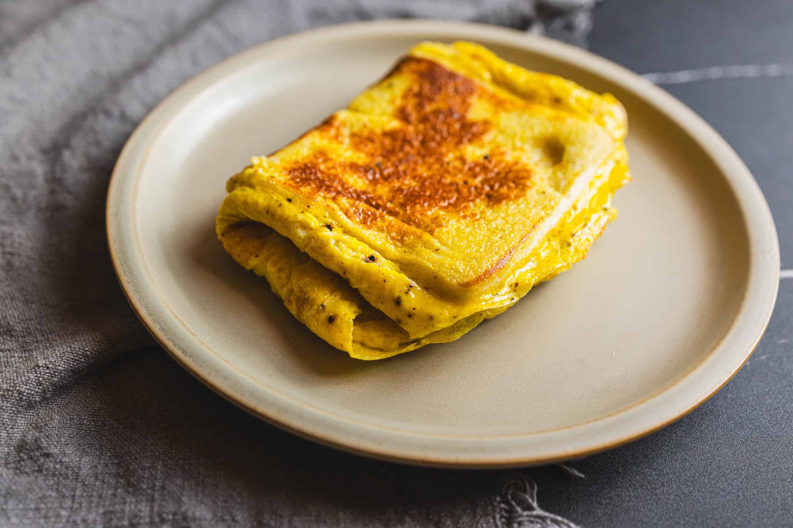 Perfectly cooked scrambled eggs with a golden-brown crust, served on a beige plate; a delicious and protein-rich breakfast option.