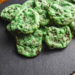 Vibrant green mint chocolate chip cookies on a dark slate serving platter, showcasing homemade baked treats with colorful chocolate chunks, perfect for dessert or snack.