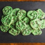 Fresh green mint chocolate chip cookies arranged on a black slate serving board, showcasing vibrant color and chocolate chunks, perfect for mint chocolate lovers and cookie recipes.