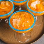 Sweet tropical fruit cocktail served in elegant glasses with blue sugar rim, garnished with ice and fruit chunks, perfect for summer drinks and party celebrations.