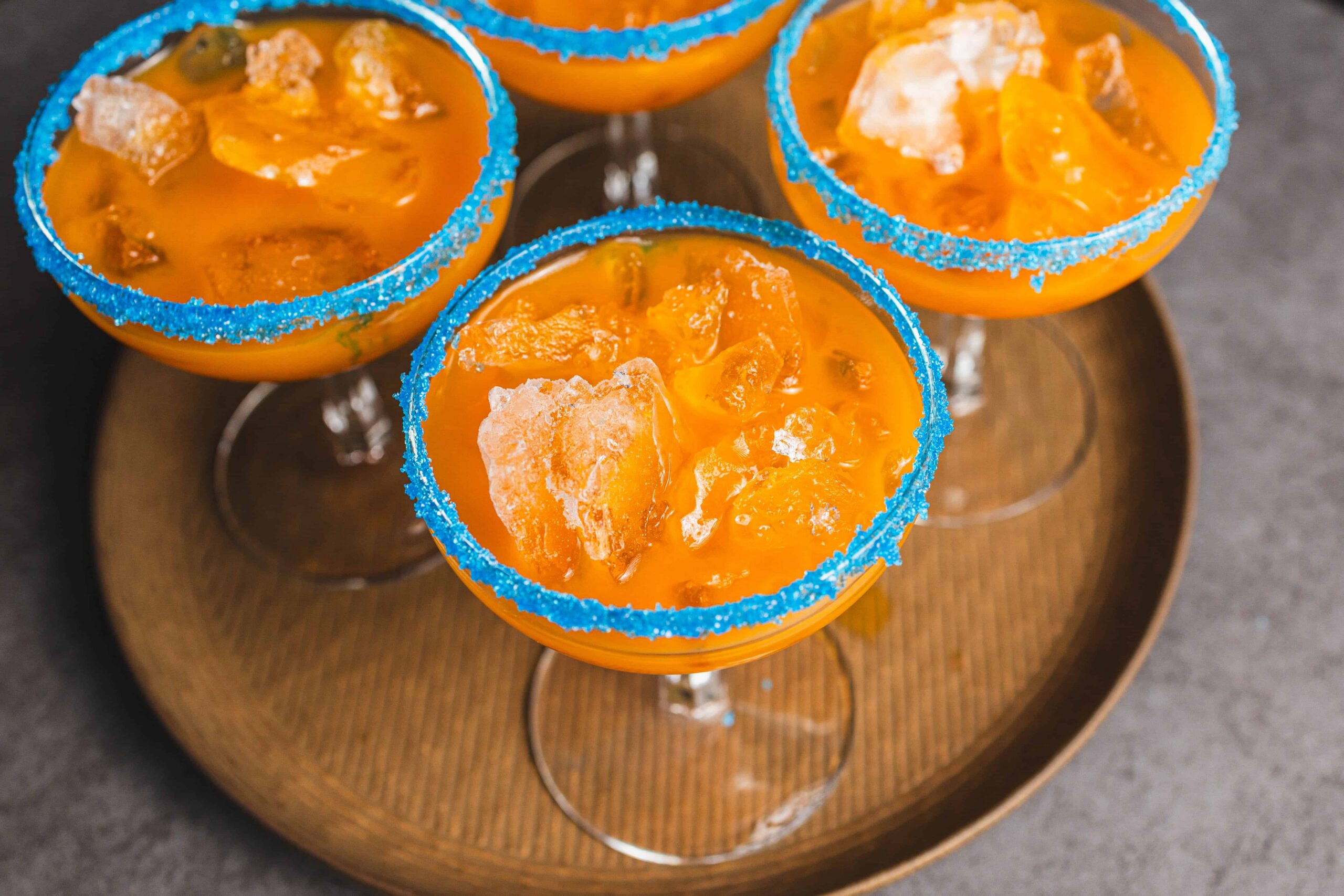 Sweet tropical fruit cocktail served in elegant glasses with blue sugar rim, garnished with ice and fruit chunks, perfect for summer drinks and party celebrations.