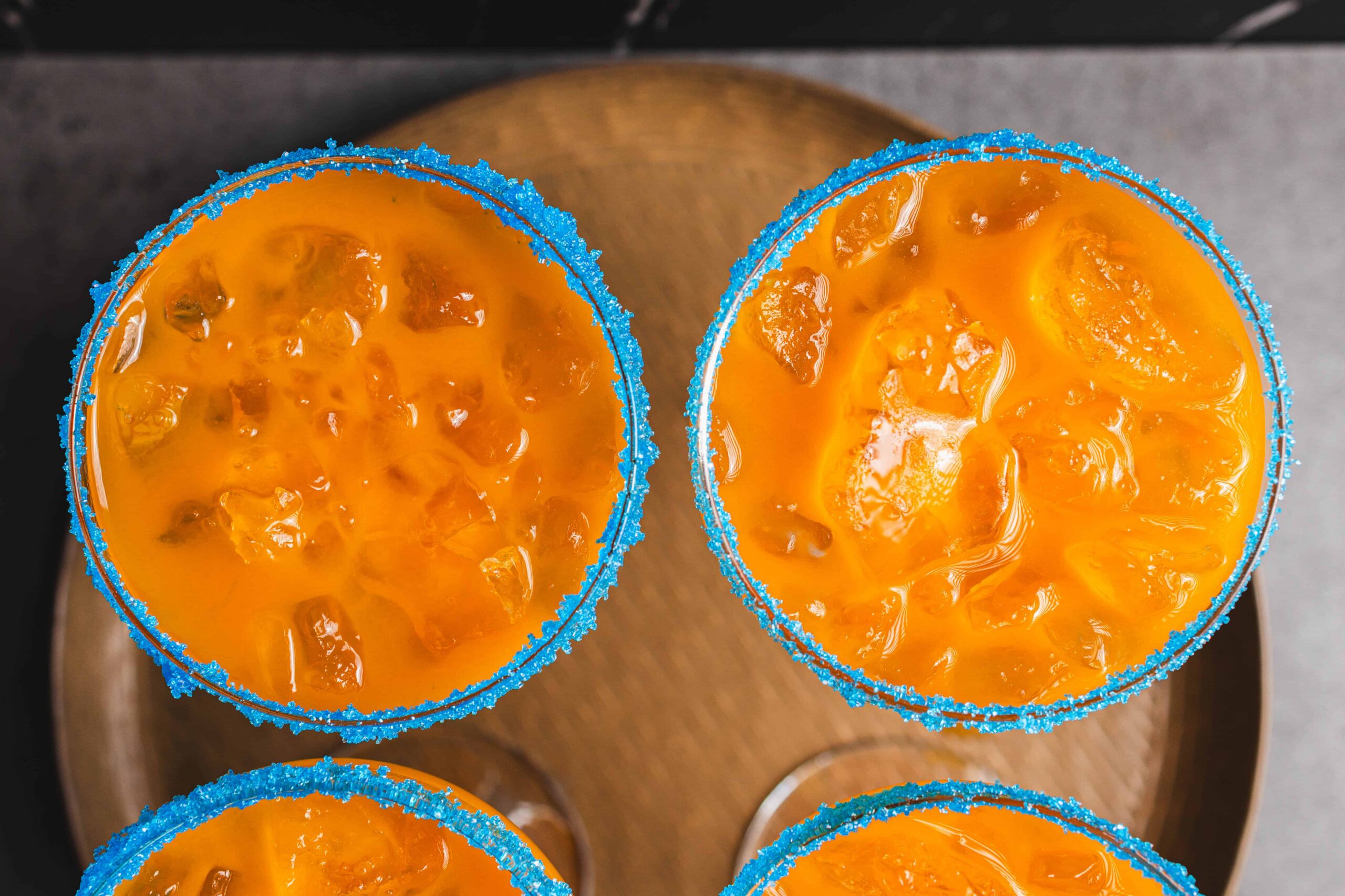 Sweet Mango Margaritas with blue sugar rim, featuring fresh mango slices and vibrant orange color, served in glasses for tropical cocktail drinks and summer party beverages.