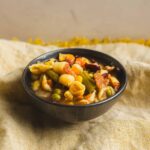 Assorted vegetable pasta salad in a black bowl on a textured beige cloth, featuring shell pasta, green beans, peas, corn, and diced vegetables. Perfect for healthy, easy-to-make vegetarian meals and side dishes.