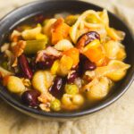 Juicy mixed vegetable pasta salad with beans, corn, and diced vegetables in a black bowl on beige fabric. A flavorful, colorful vegetarian dish perfect for lunch or dinner.