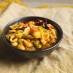 Creamy mixed vegetable pasta salad in a black bowl, garnished with herbs, served on a rustic cloth, perfect for healthy meal ideas and vegetarian recipes.