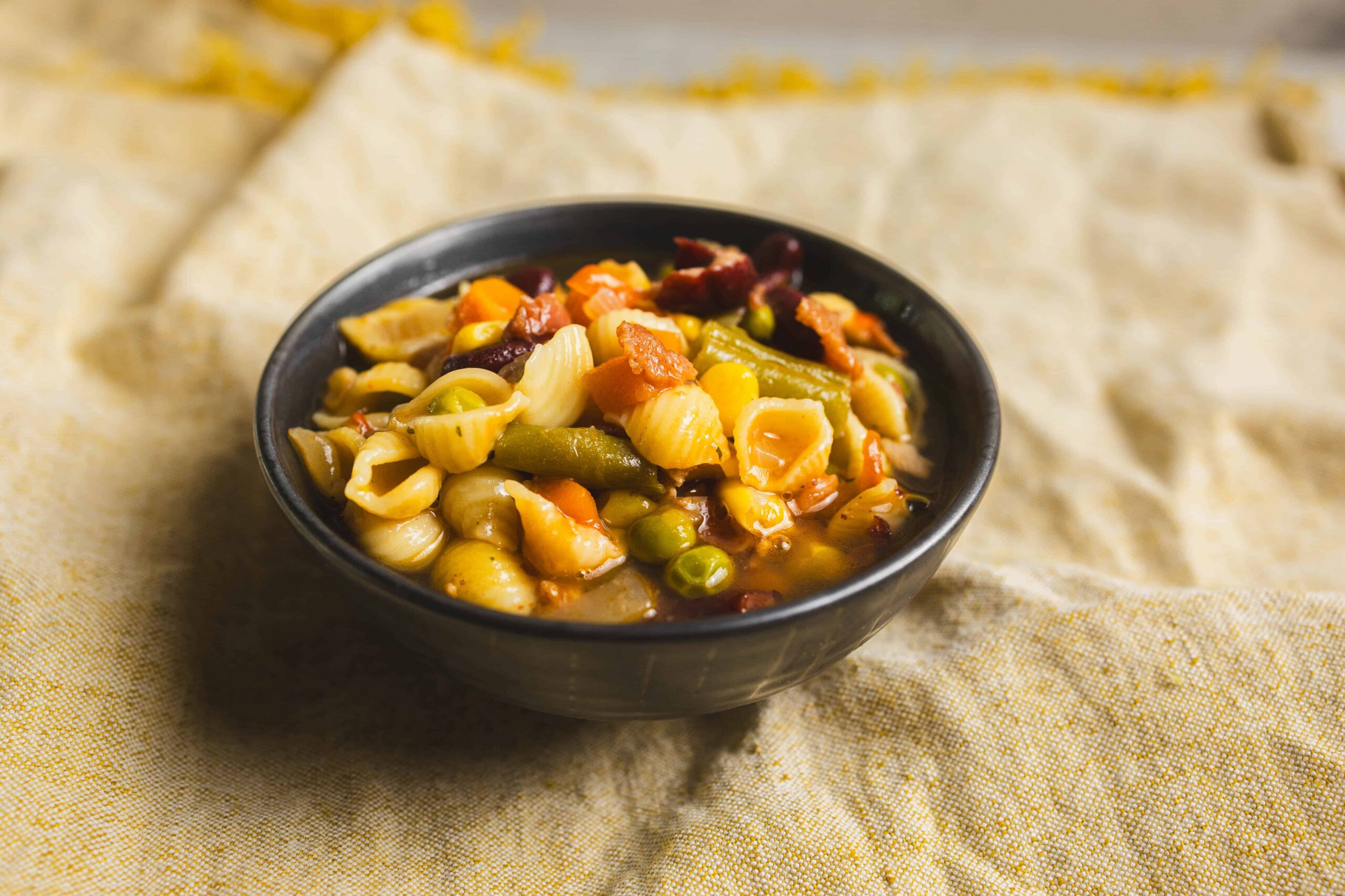 Creamy mixed vegetable pasta salad in a black bowl, garnished with herbs, served on a rustic cloth, perfect for healthy meal ideas and vegetarian recipes.