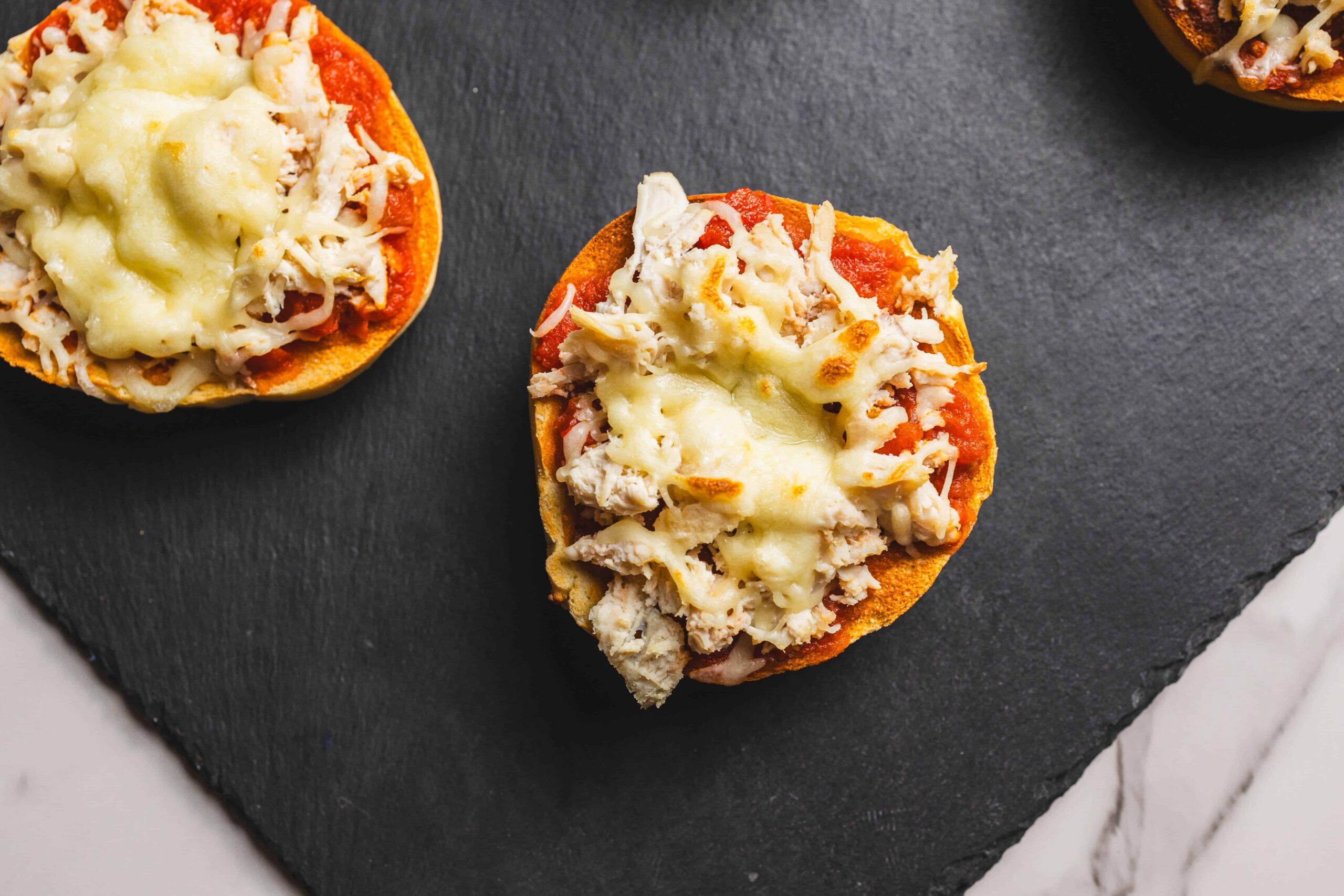 Crispy mini pizza stuffed peppers topped with melted cheese and shredded chicken on black slate serving platter.