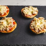 Golden baked stuffed mini bell peppers topped with shredded chicken and melted cheese, served on a black slate platter. Perfect for appetizer recipes or quick party snacks.