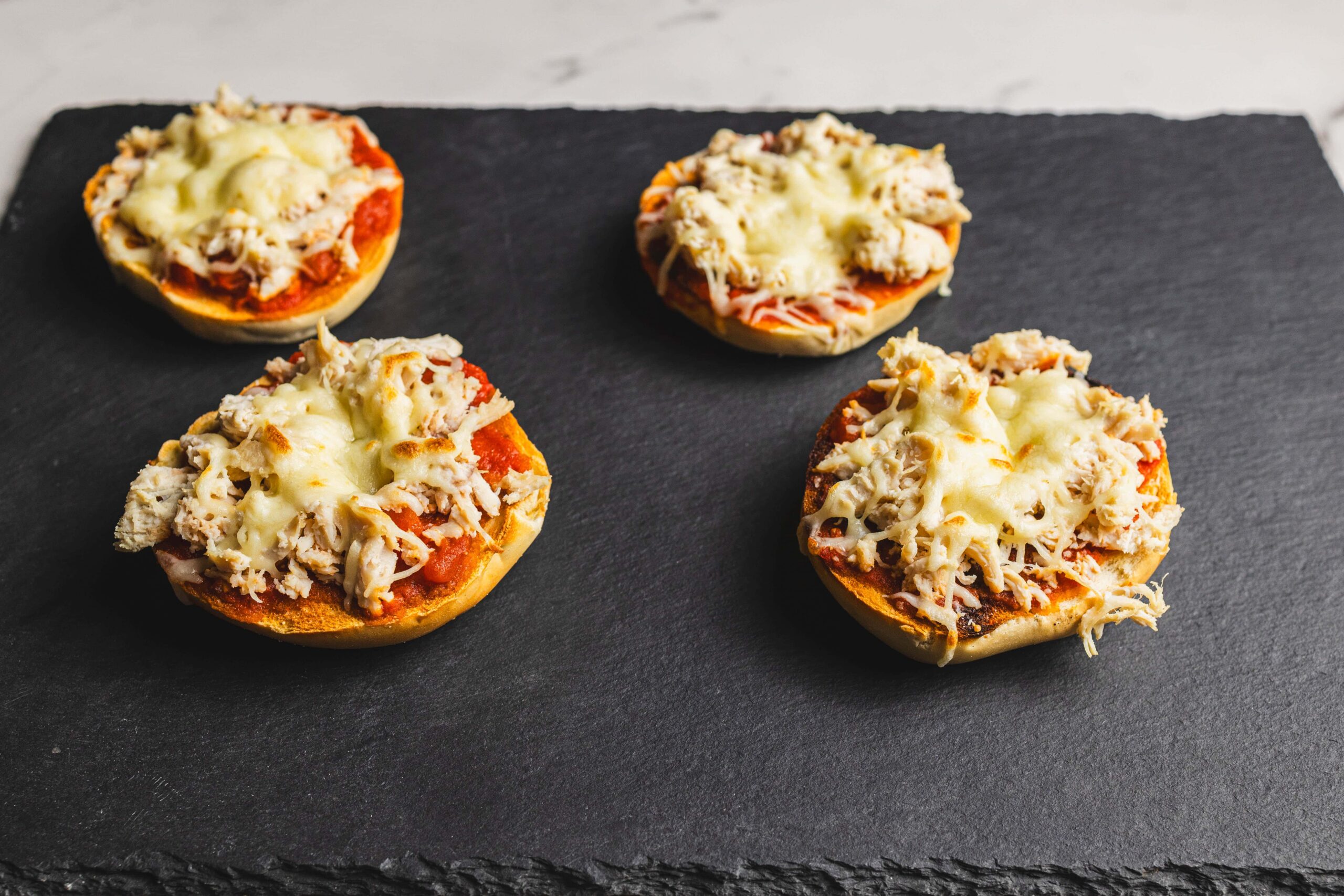 Golden baked stuffed mini bell peppers topped with shredded chicken and melted cheese, served on a black slate platter. Perfect for appetizer recipes or quick party snacks.
