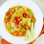Colorful vegetable soup with cherry tomatoes, carrots, celery, and chopped vegetables served in a white bowl, perfect for healthy eating and nutritious meals.