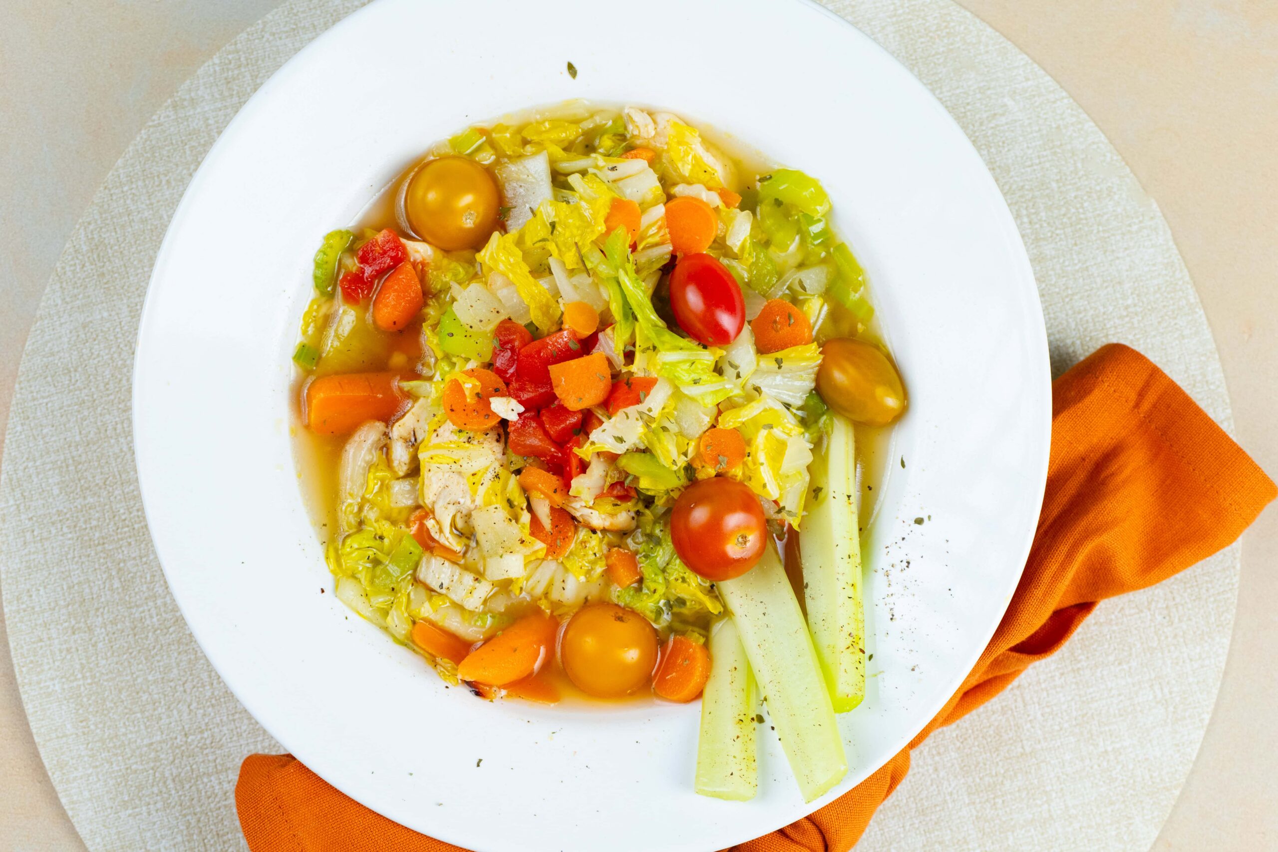 Colorful vegetable soup with cherry tomatoes, carrots, celery, and chopped vegetables served in a white bowl, perfect for healthy eating and nutritious meals.