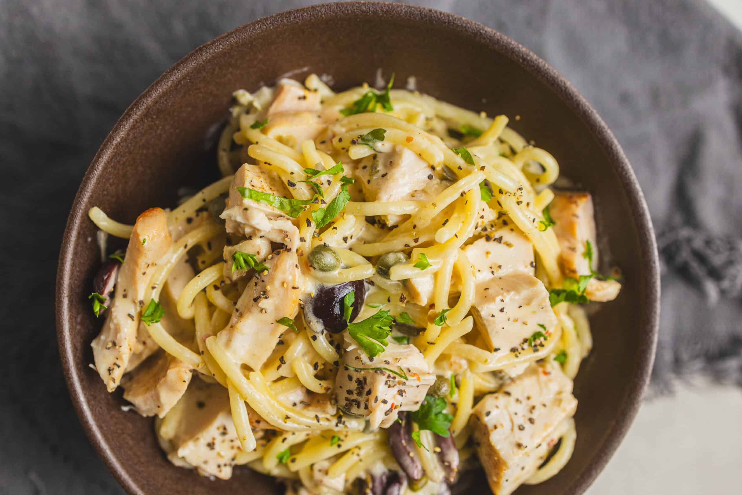 Creamy chicken pasta with herbs, vegetables, and black pepper in a brown bowl, ready to serve.