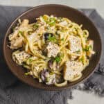 Creamy chicken and mushroom pasta with herbs in a rustic bowl on a grey cloth.