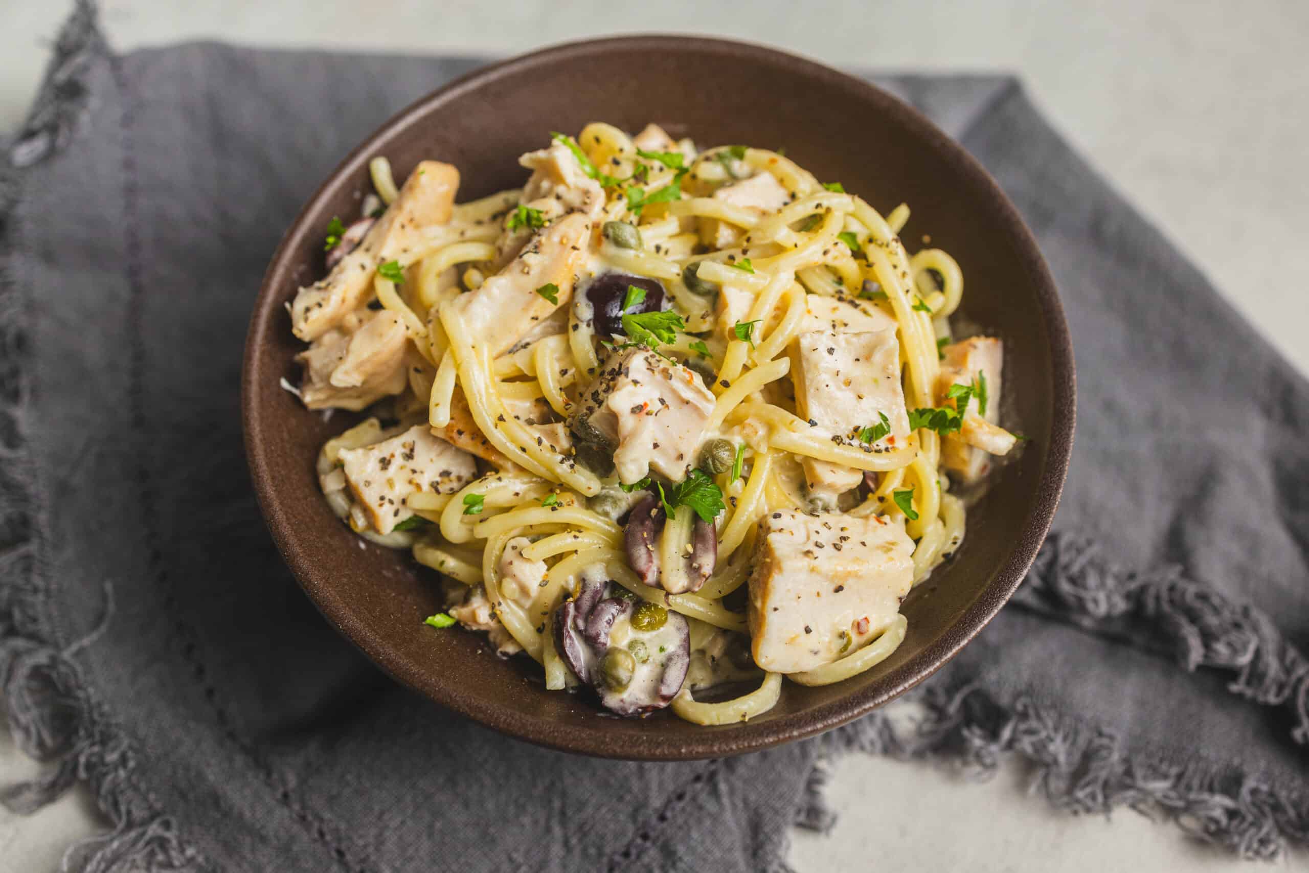 Creamy chicken and mushroom pasta with herbs in a rustic bowl on a grey cloth.