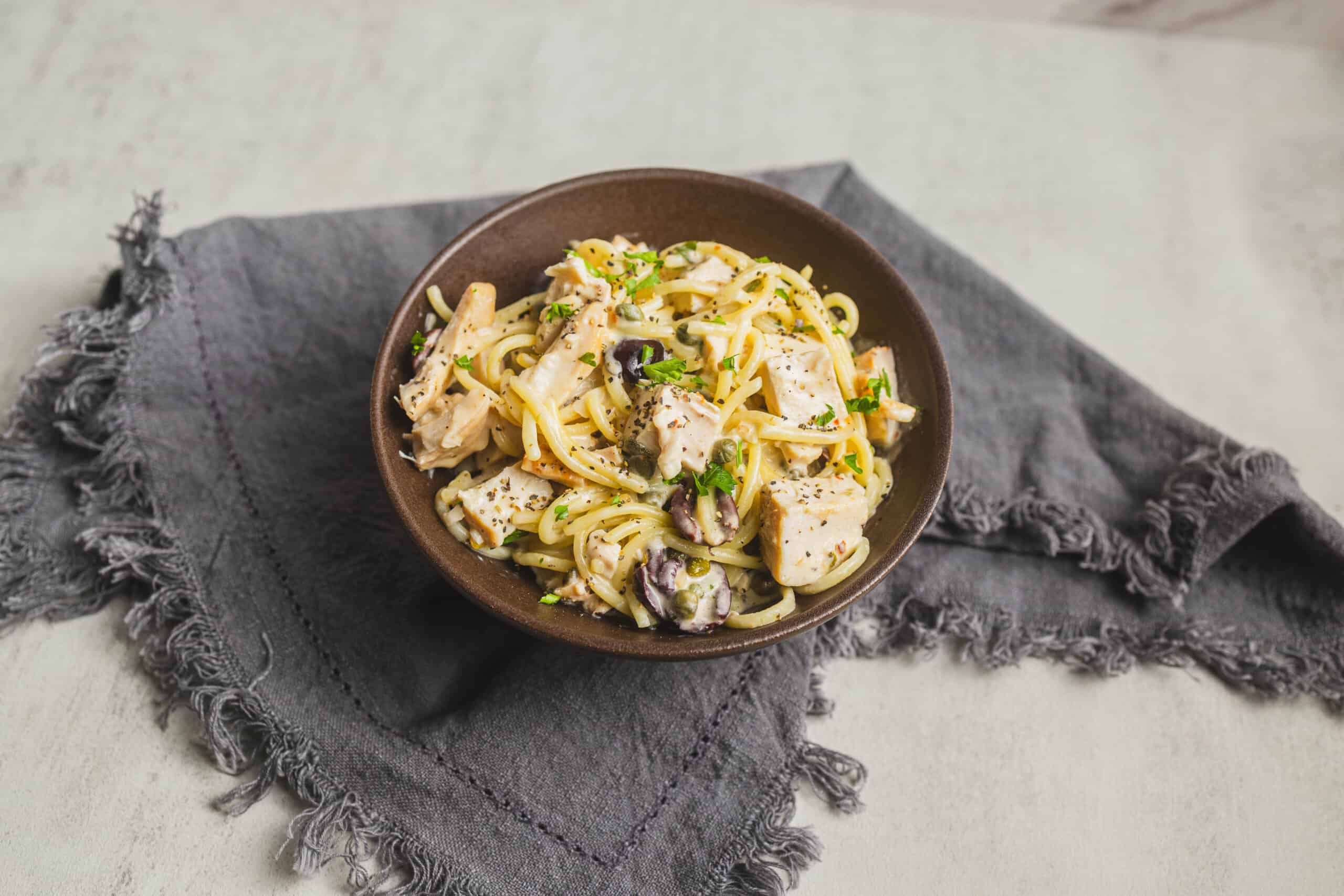 Creamy chicken and mushroom pasta in a brown bowl, garnished with herbs, served on a rustic gray cloth. Perfect for easy dinner recipes and comfort food lovers.