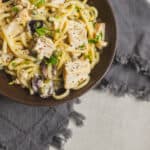 Creamy chicken pasta with herbs, black olives, and capers in a savory white sauce served in a rustic bowl. Perfect comfort food recipe for dinner, featuring tender chicken, spaghetti, and flavorful seasonings.