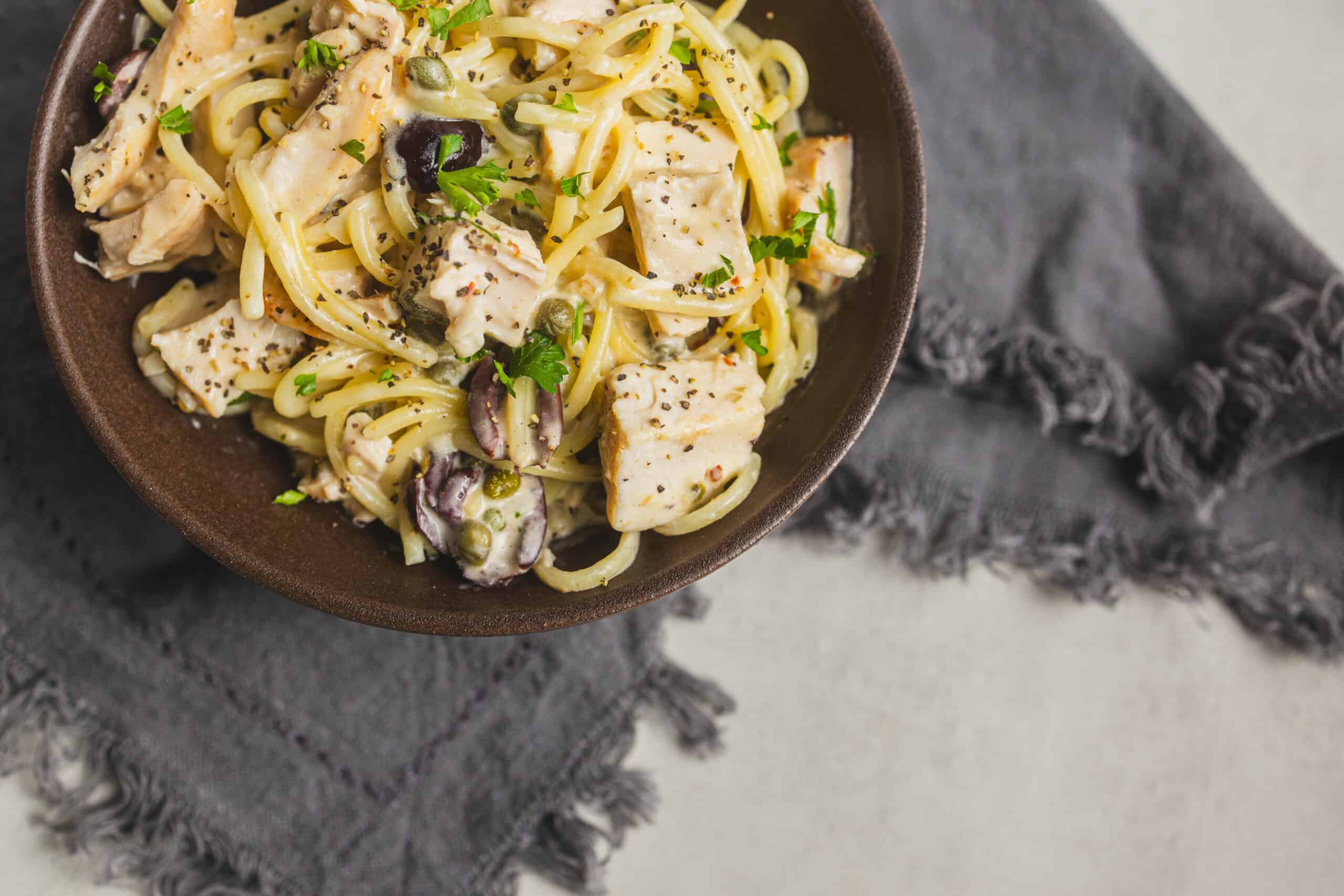 Creamy chicken pasta with herbs, black olives, and capers in a savory white sauce served in a rustic bowl. Perfect comfort food recipe for dinner, featuring tender chicken, spaghetti, and flavorful seasonings.
