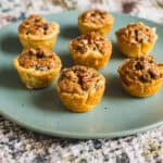 Cream cheese stuffed mini muffins with a crumb topping on a light blue plate, perfect for breakfast or snack, featuring a golden crust and moist texture.