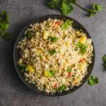 Steamed vegetable fried rice garnished with fresh cilantro in a black bowl on a gray textured background.