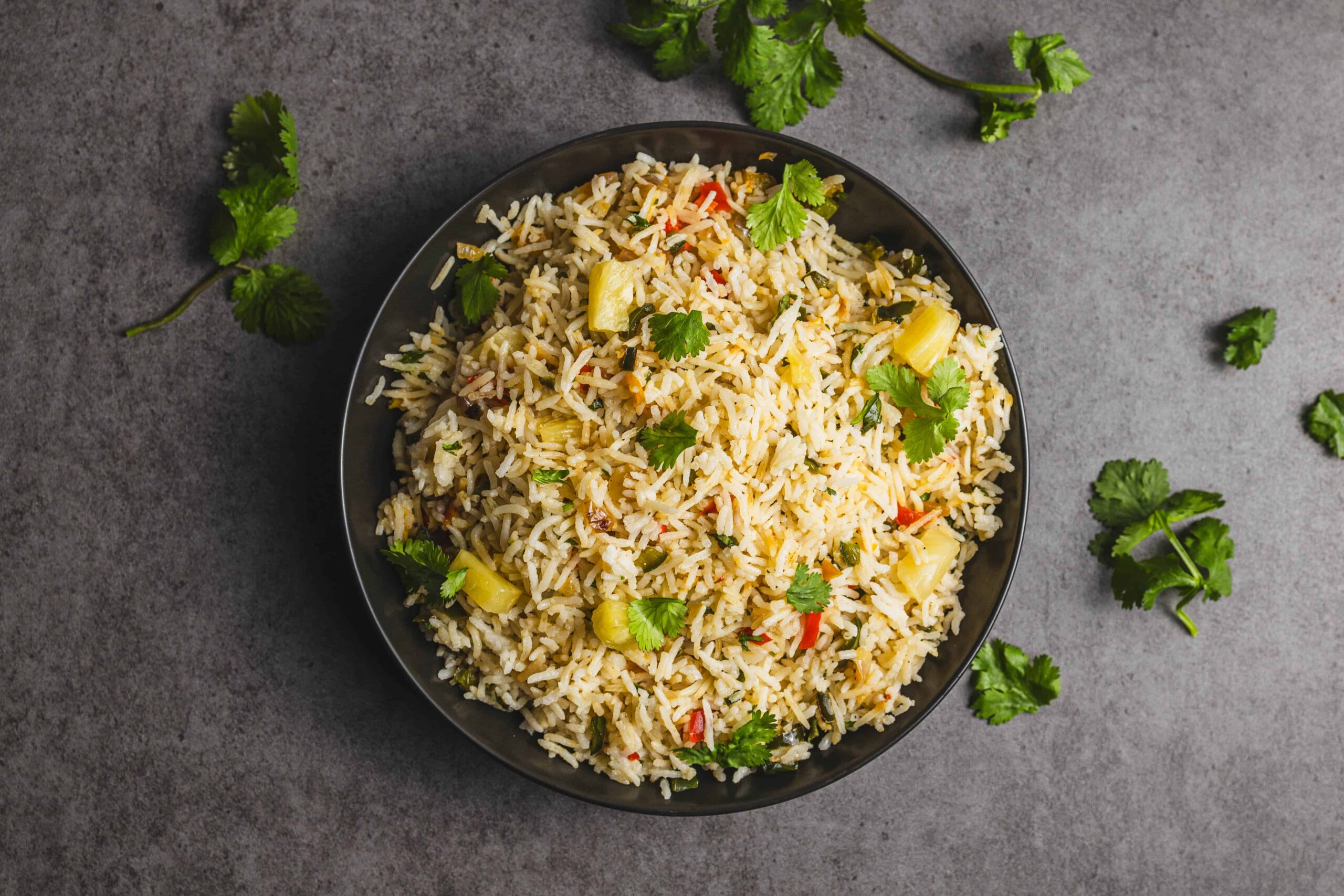 Steamed vegetable fried rice garnished with fresh cilantro in a black bowl on a gray textured background.