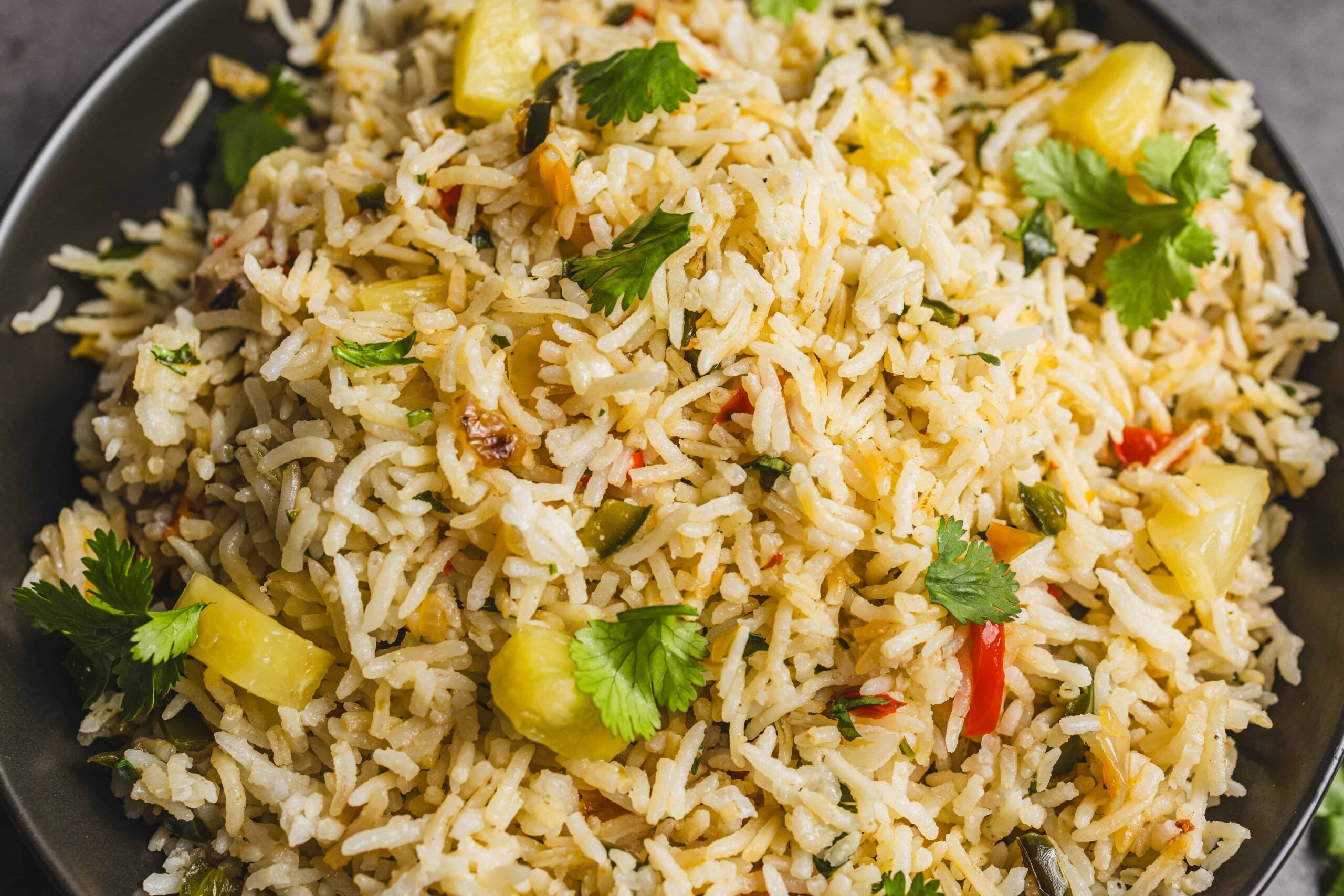 Fragrant vegetable fried rice with pineapple, cilantro, and colorful bell peppers served in a black bowl. Perfect for a quick, healthy, and flavorful meal or side dish.