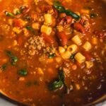 Savory homemade beef and vegetable chili in a pot with tomatoes, ground beef, kidney beans, corn, and spices, ready to serve as a hearty, flavorful meal.