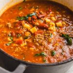 Beef and bean chili soup in a pot with ground beef, kidney beans, corn, tomatoes, and spices. Hearty and flavorful chili perfect for cold weather, served in a rustic kitchen setting.