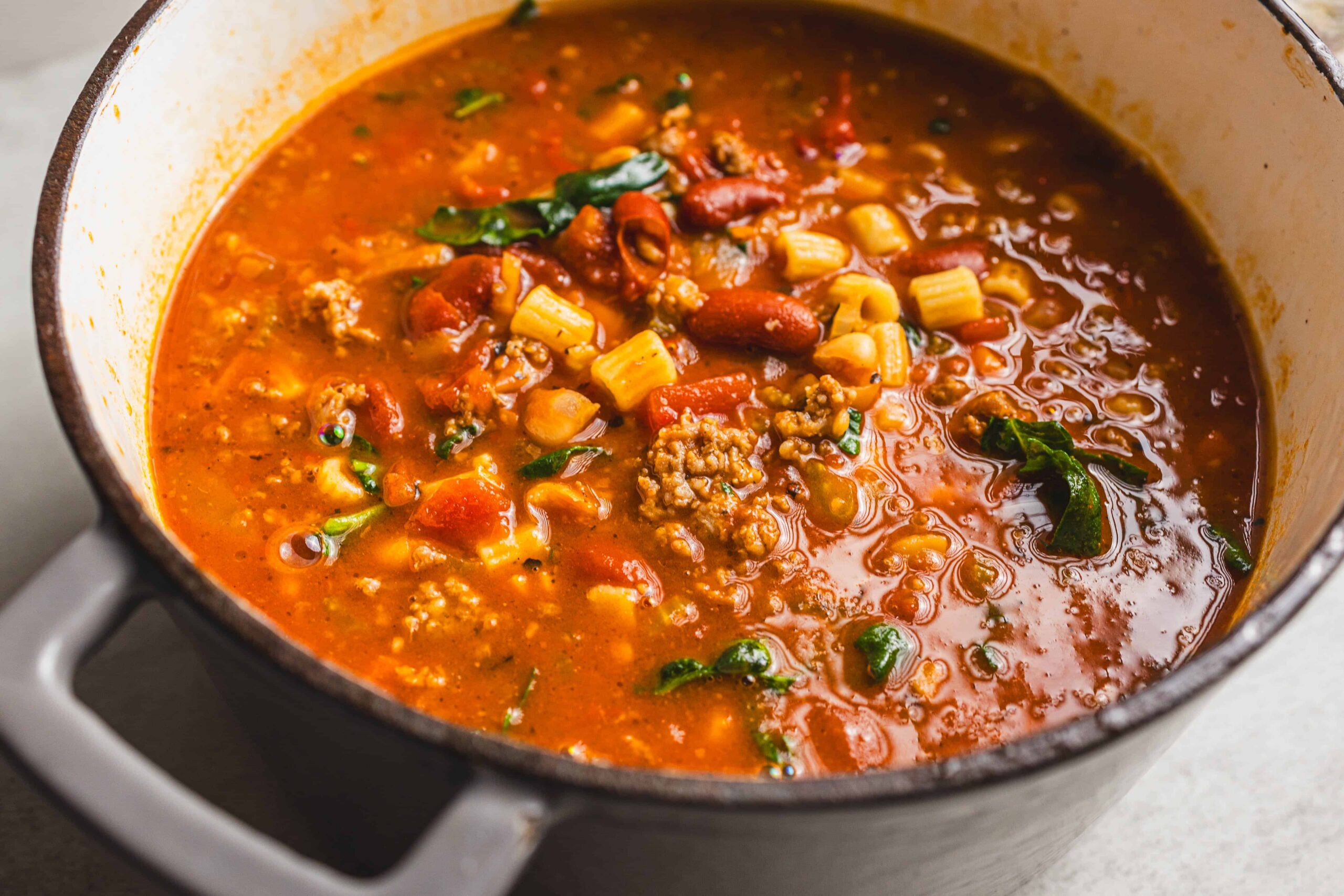 Beef and bean chili soup in a pot with ground beef, kidney beans, corn, tomatoes, and spices. Hearty and flavorful chili perfect for cold weather, served in a rustic kitchen setting.