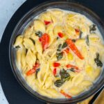 Creamy pasta shell soup with vegetables and herbs, served in a black bowl, perfect for cozy meals and comfort food.