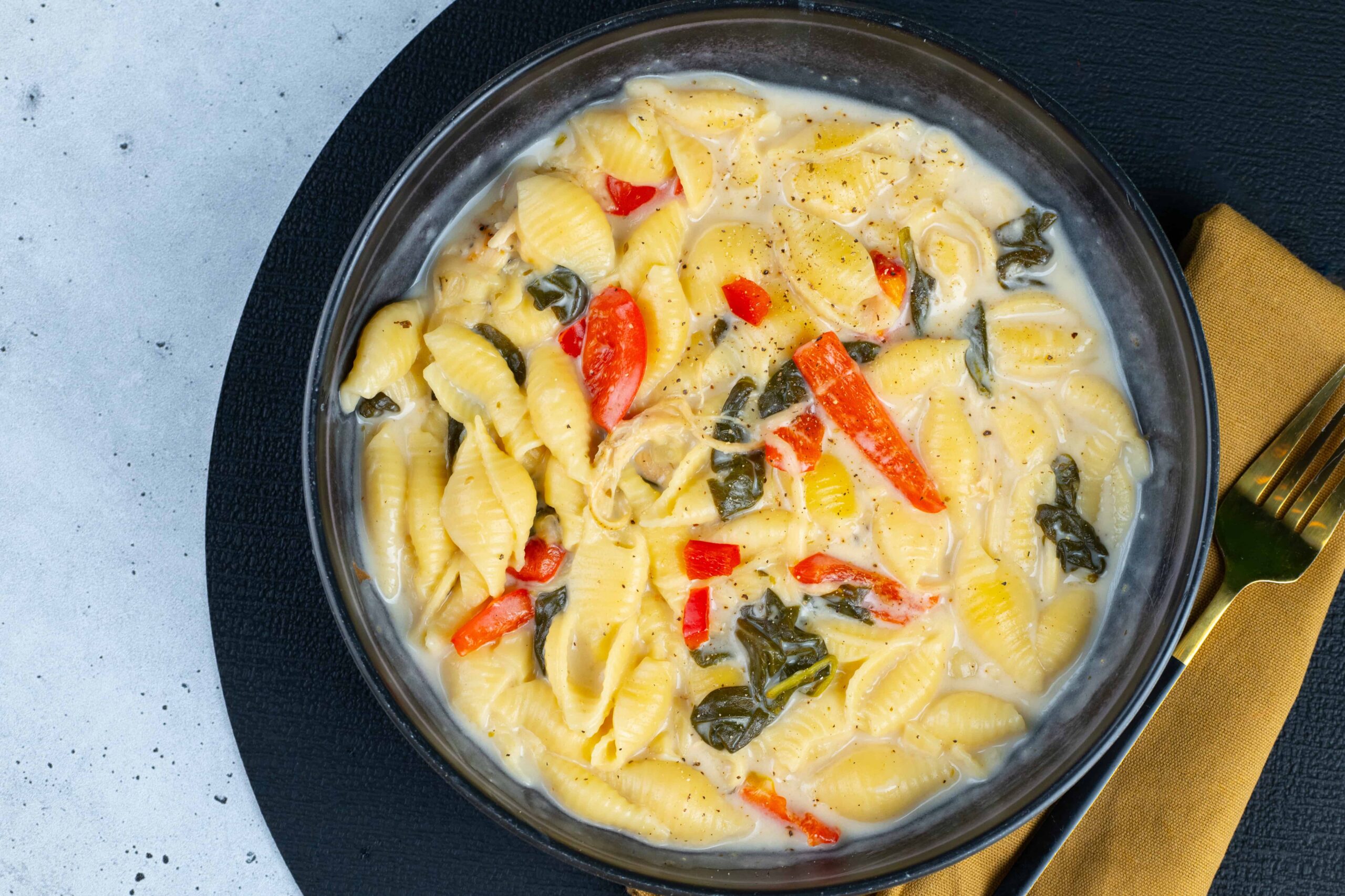 Creamy pasta shell soup with vegetables and herbs, served in a black bowl, perfect for cozy meals and comfort food.