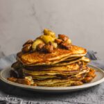 Fluffy stack of pancakes topped with caramelized bananas and walnuts, served on a rustic plate for a delicious breakfast or brunch.