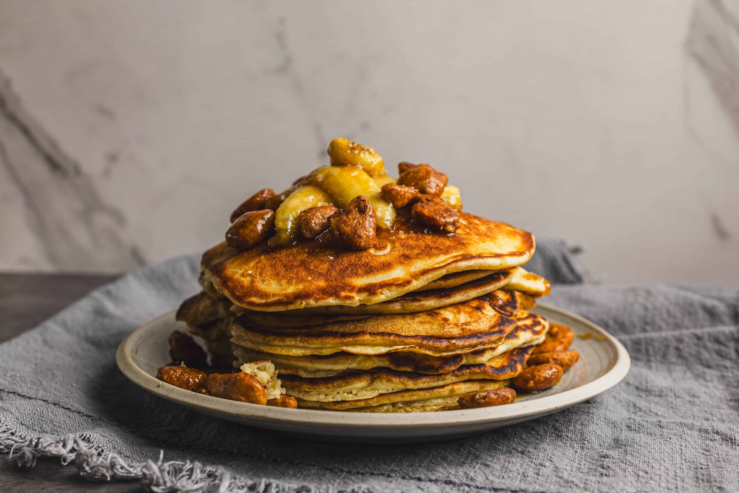 Fluffy stack of pancakes topped with caramelized bananas and walnuts, served on a rustic plate for a delicious breakfast or brunch.