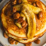 Sweet potato pancake topped with caramelized bananas, pecans, and syrup, served on a white plate. Perfect for breakfast or brunch, featuring a flavorful combination of healthy ingredients and rich toppings.