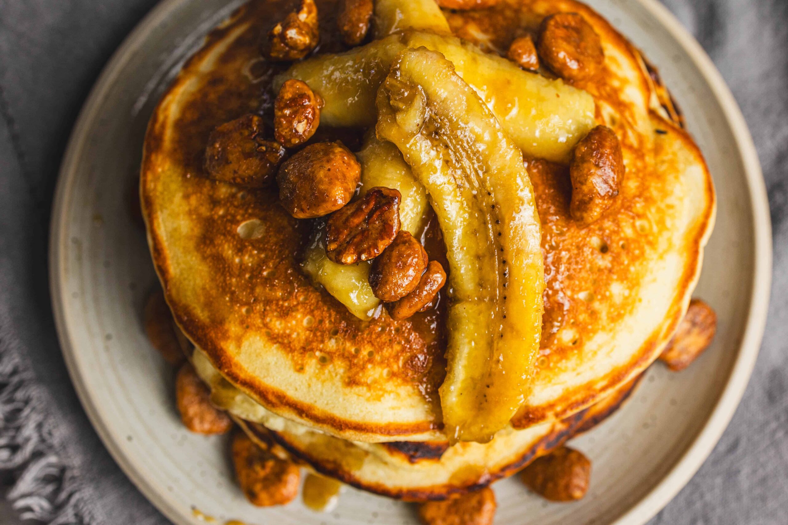 Sweet potato pancake topped with caramelized bananas, pecans, and syrup, served on a white plate. Perfect for breakfast or brunch, featuring a flavorful combination of healthy ingredients and rich toppings.