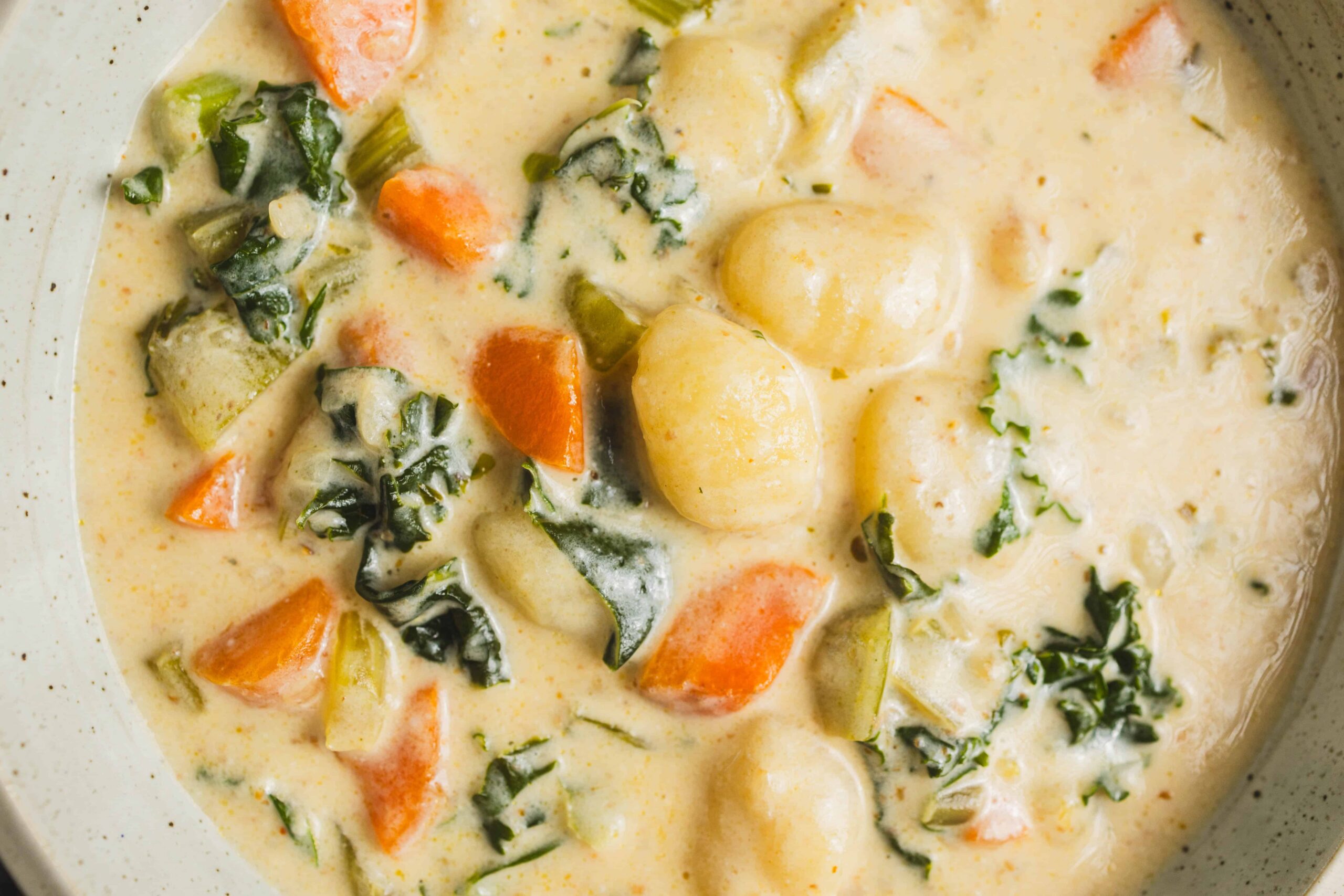 Creamy vegetable potato soup with carrots, kale, and herbs in a close-up shot.