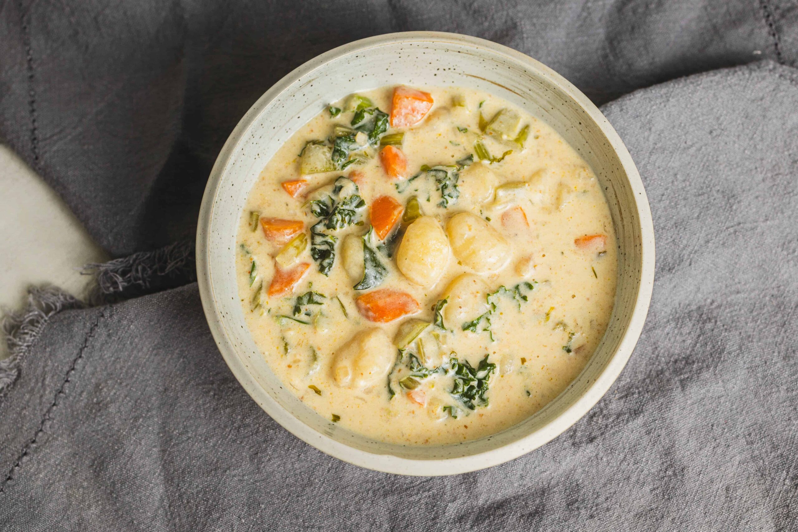Creamy vegetable chicken stew in a white bowl, featuring carrots, potatoes, spinach, and tender chicken pieces, served on a rustic gray cloth, perfect for comforting homemade dinner recipes.