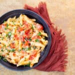 Creamy tomato chicken pasta with fresh herbs in a dark bowl on a textured surface.