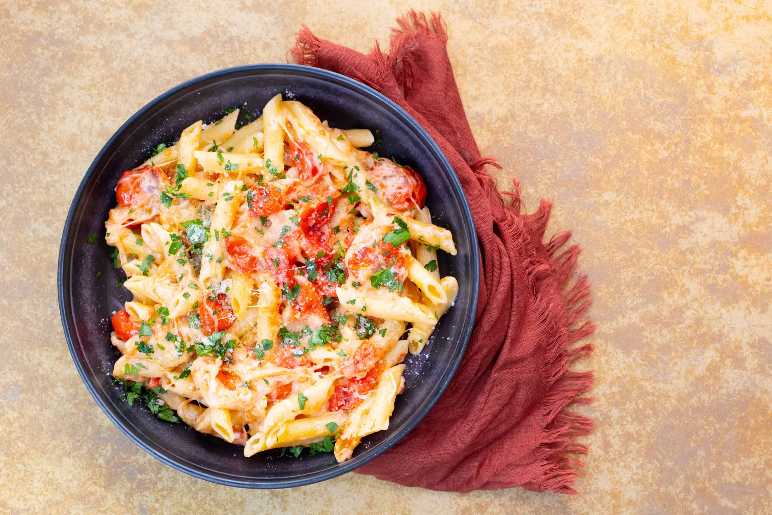 Creamy tomato chicken pasta with fresh herbs in a dark bowl on a textured surface.