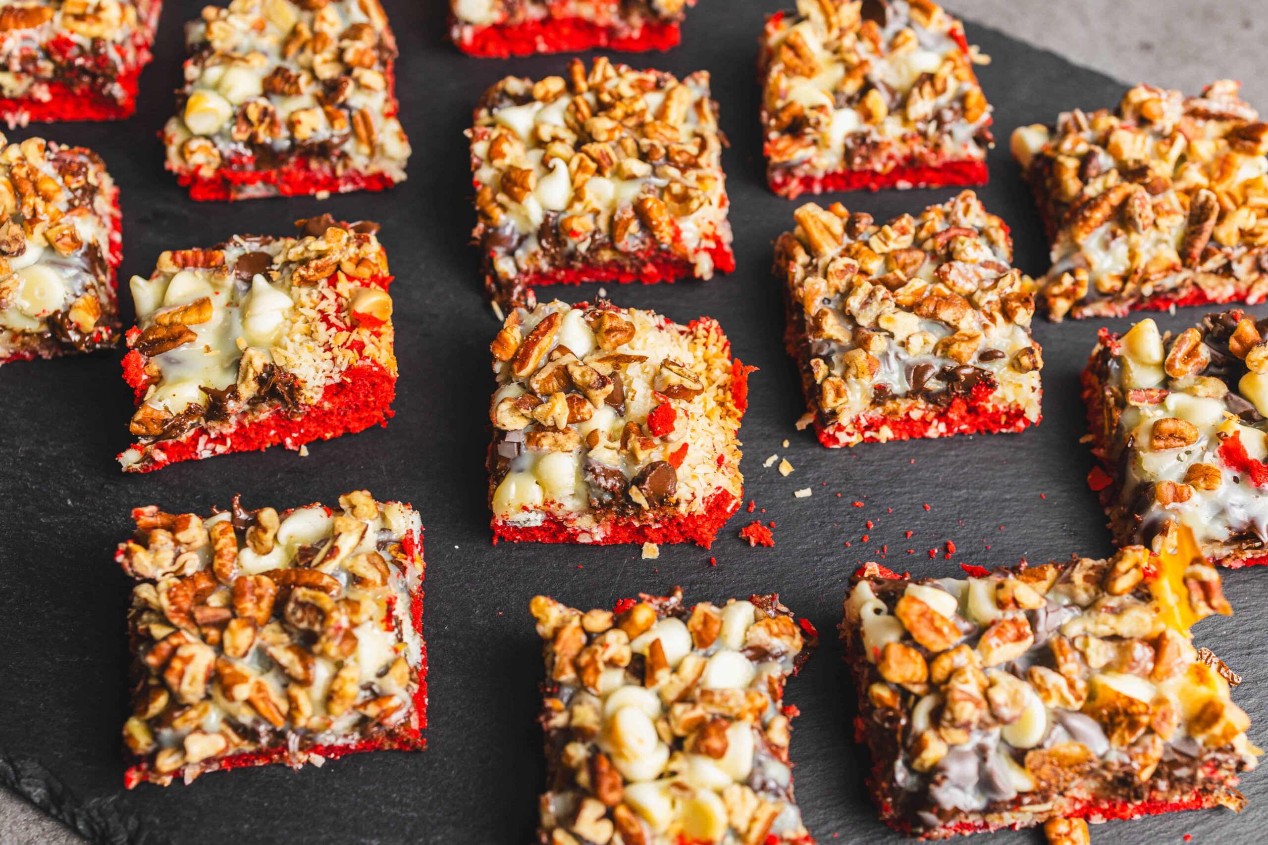 Sweet snowball dessert bars topped with white chocolate, chopped pecans, and a layered red velvet base, perfect for holiday treats and sweet snack recipes.