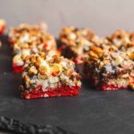 Red velvet no-bake dessert bars topped with chopped nuts and white chocolate on a black slate serving board.