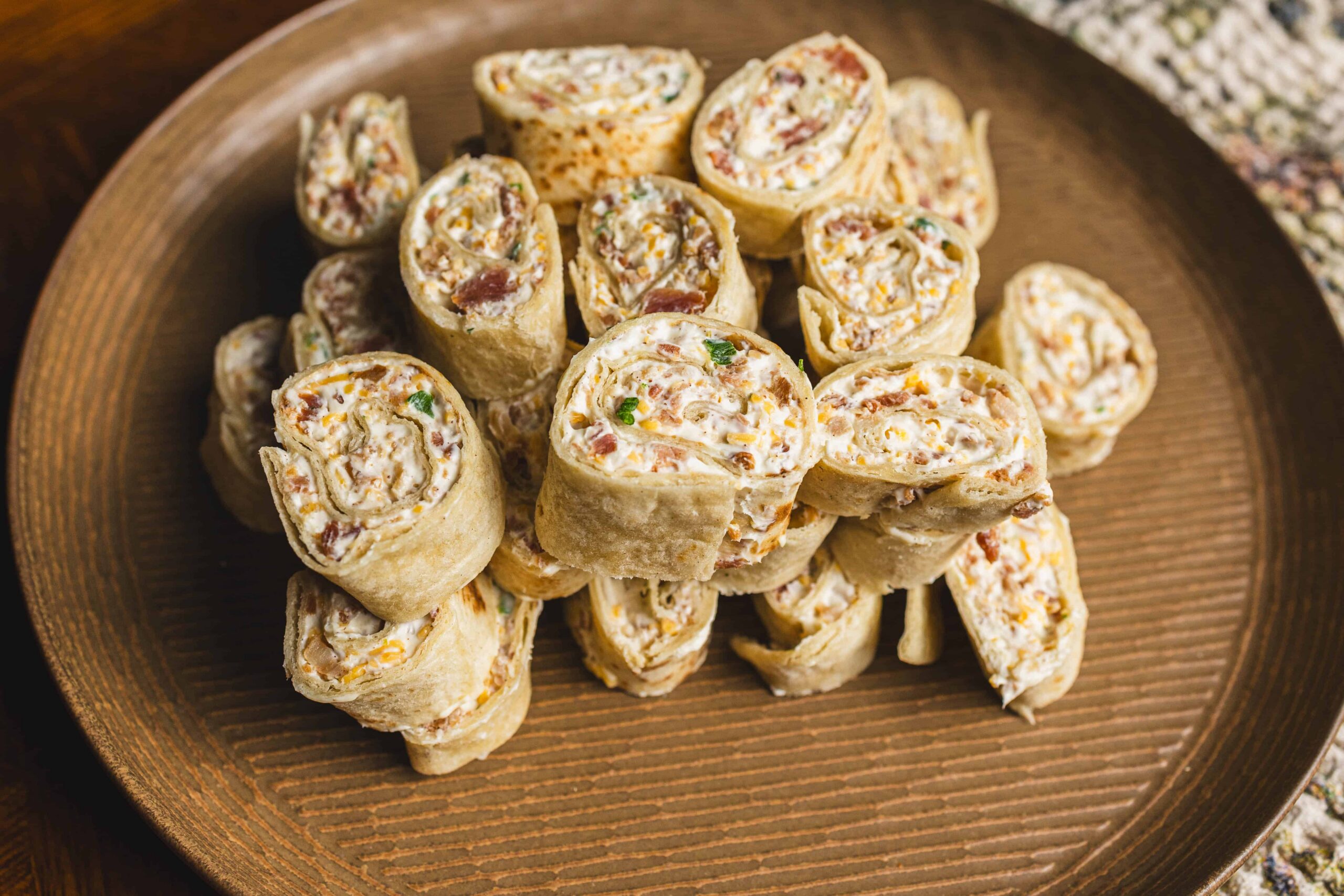 Scrambled egg and bacon breakfast burritos sliced into spirals, arranged on a round wooden plate. Perfect for quick breakfast ideas and savory brunch recipes.