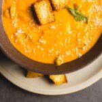 Creamy pumpkin soup garnished with toasted croutons and a sprinkle of grated cheese, served in a rustic bowl, perfect for fall or cozy mealtime.