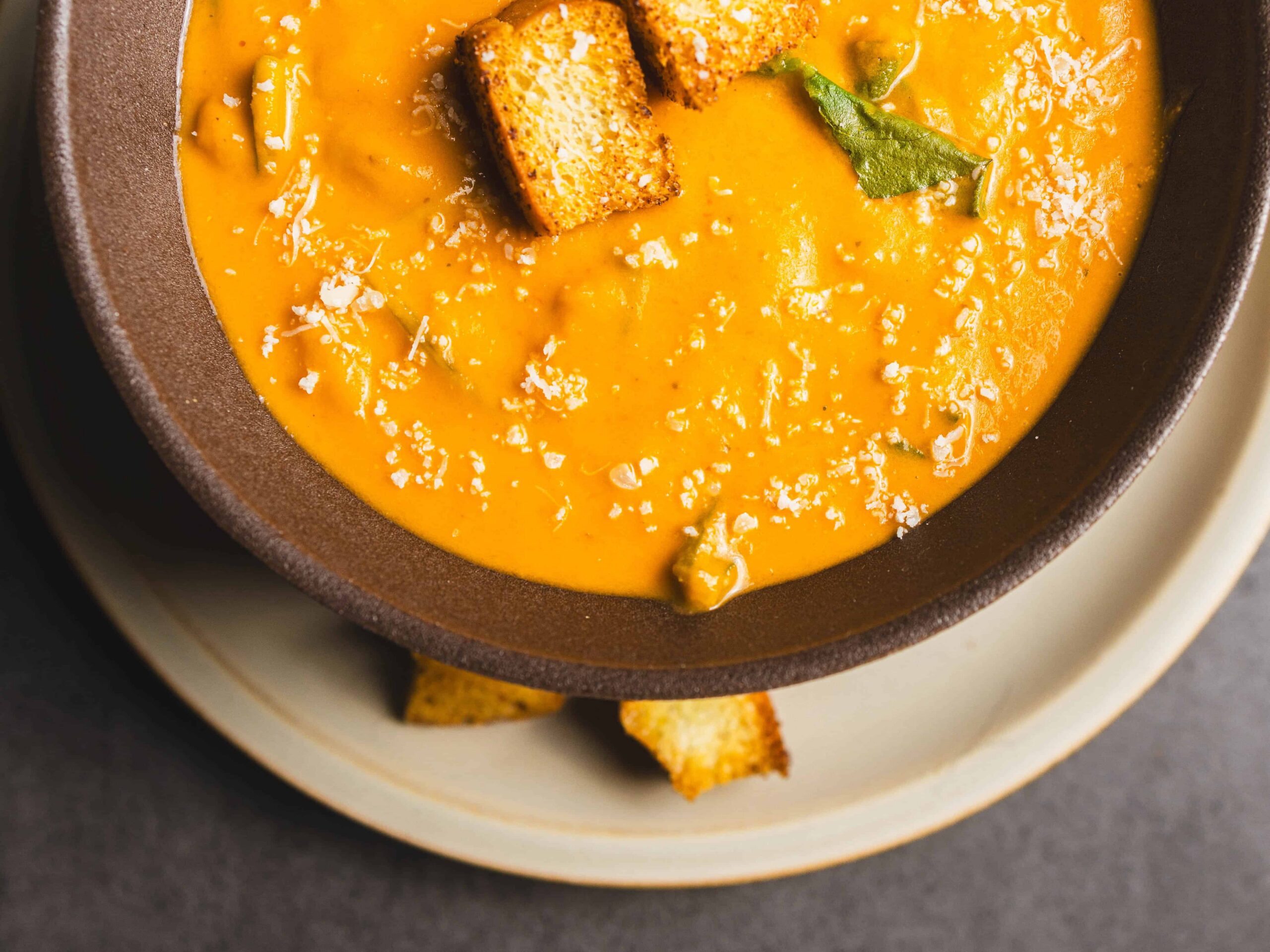 Creamy pumpkin soup garnished with toasted croutons and a sprinkle of grated cheese, served in a rustic bowl, perfect for fall or cozy mealtime.